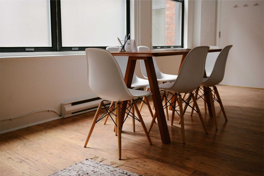 Wooden dining table with white shell chairs in a bright room with wide-plank floor
