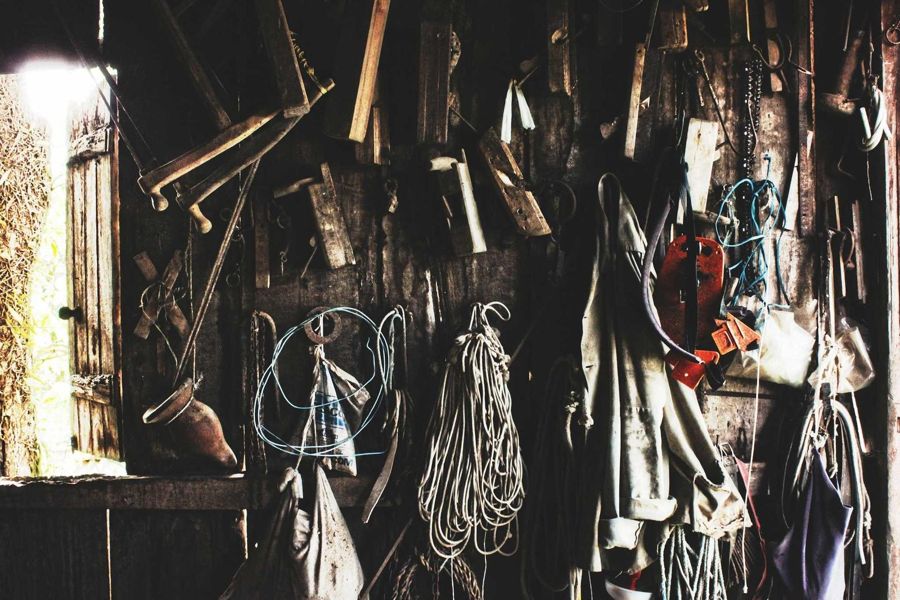 Dim workshop wall hung with tools, rope, aprons and an open shutter letting in light